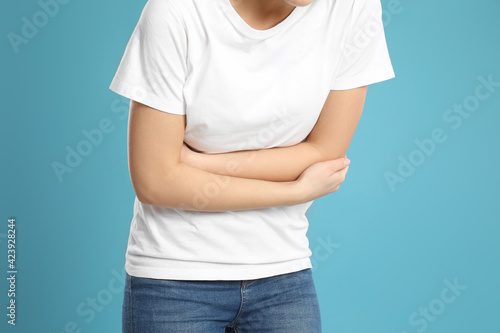 Fotografie Young woman suffering from stomach ache on light blue background, closeup