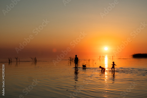 Silhouette of a big family walking on the lake at sunset. Concept of traveling family and enjoying the outdoors and the nature.