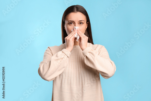 Fotografie Young woman with tissue suffering from runny nose on light blue background