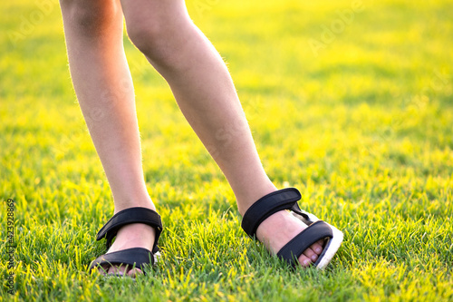Closeup of young child girl legs standing on green grass lawn on warm summer evening.
