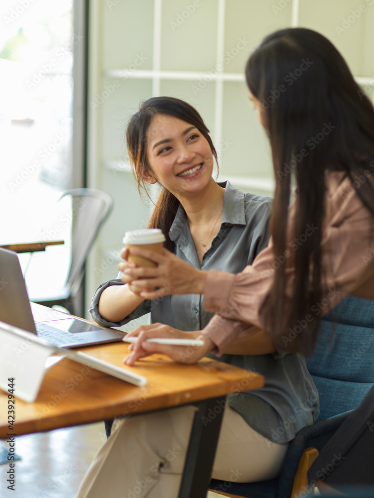 Kindly female office worker giving coffee to her colleague while working together Kindly female office worker giving coffee to her colleague while working together