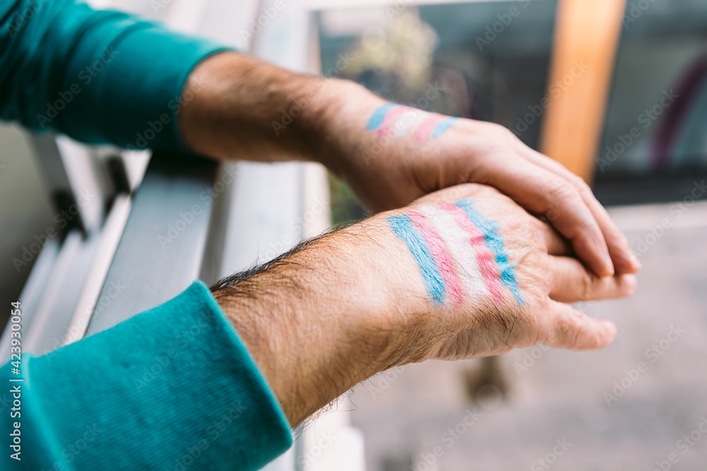 Transsexual man rests his hands with the transsexual flag painted on them, on a railing
