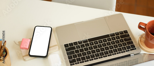 Workspace with laptop, smartphone, mug and stationery on white table