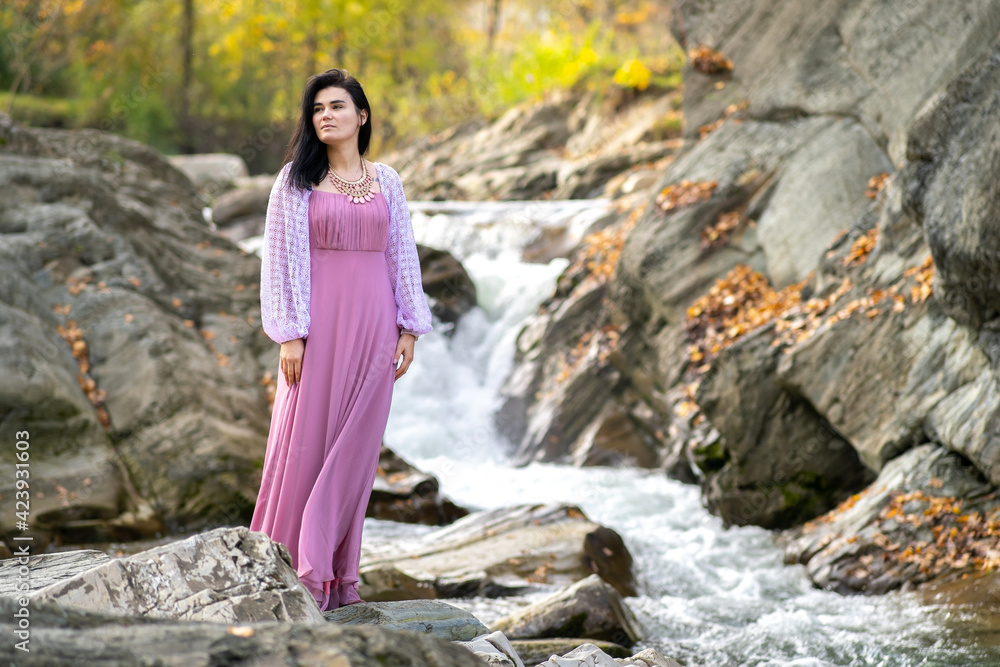 Young pretty woman in long fashionable dress standing near small mountain river with fast moving water. Young pretty woman in long fashionable dress standing near small mountain river with fast moving water.