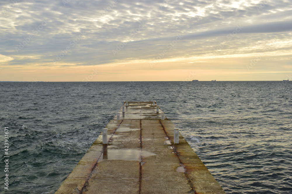 concrete pier, sea view, horizon, sky in clouds. Dream of an empty concrete pier concept of rest, vacation, summer, trip to the sea. old pier. Image of an outfall with waves and clouds at sunrise