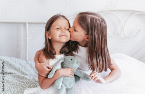 A little girl kisses her little sister on the cheek. Girls resting in the children's bedroom