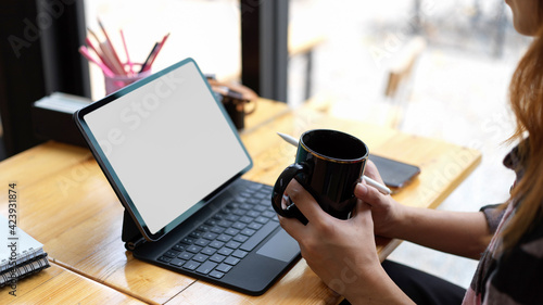 Female holding coffee cup while working on her project with blank screen tablet