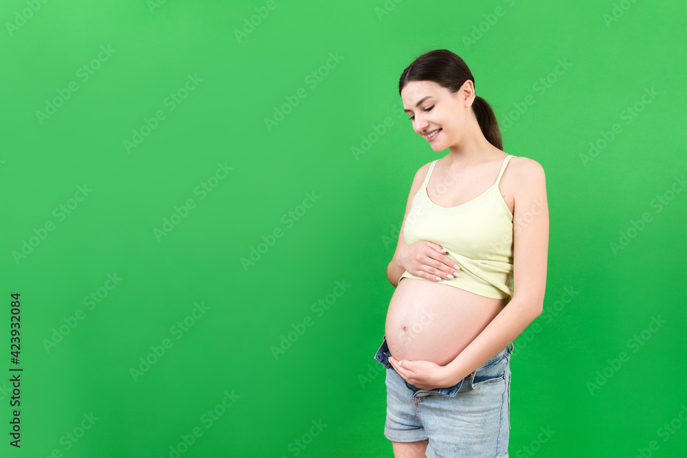 pregnant woman in unzipped jeans showing her naked belly at colorful background with copy space. Baby expecting concept pregnant woman in unzipped jeans showing her naked belly at colorful background with copy space. Baby expecting concept