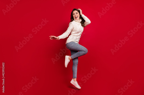 Full length photo of pretty shiny young woman dressed white sweater jumping high arm head isolated red color background