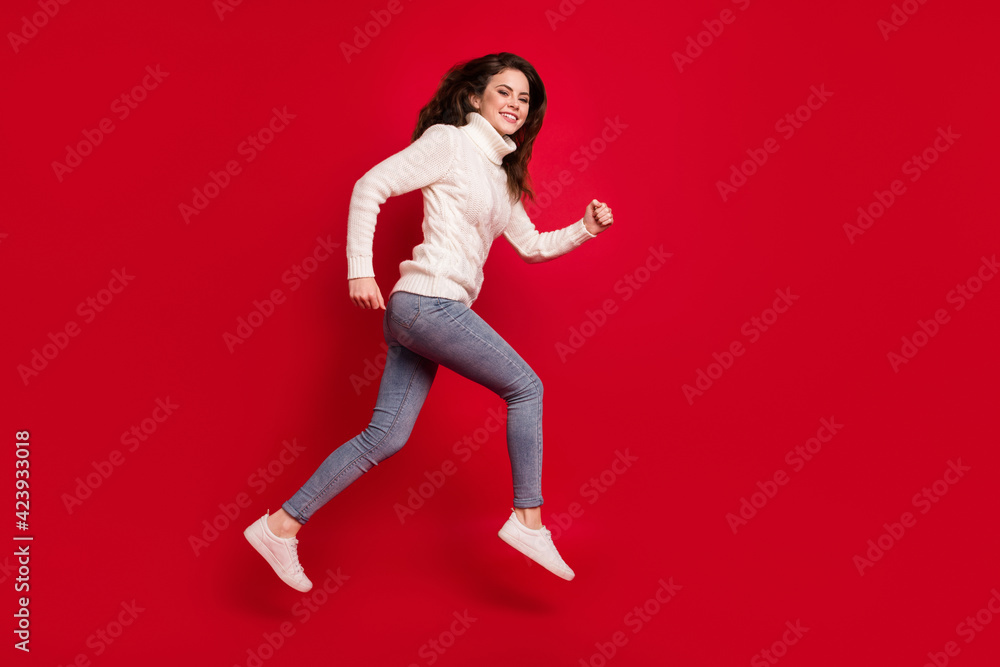 Full length photo of pretty sweet young woman dressed white sweater running fast jumping high isolated red color background Full length photo of pretty sweet young woman dressed white sweater running fast jumping high isolated red color background