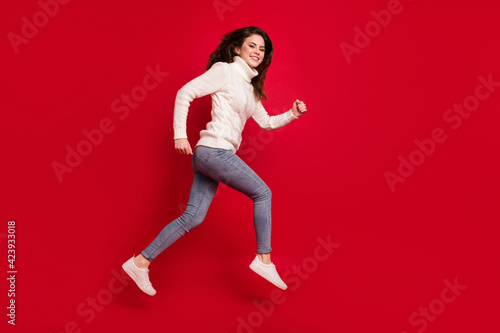 Full length photo of pretty sweet young woman dressed white sweater running fast jumping high isolated red color background