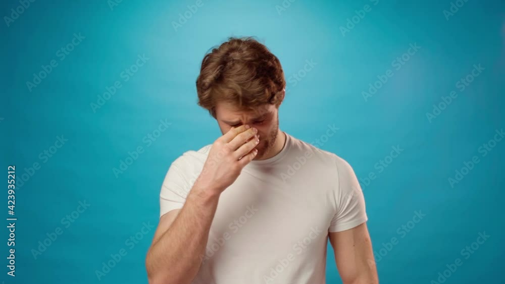 Tired young man rubbing his eyes, portrait against blue background Tired young man rubbing his eyes, portrait against blue background
