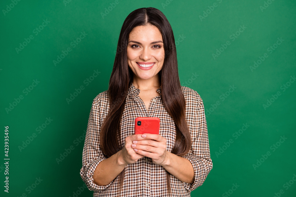 Photo of girl hold cellphone look camera shiny smile wear checkered shirt isolated green color background Photo of girl hold cellphone look camera shiny smile wear checkered shirt isolated green color background