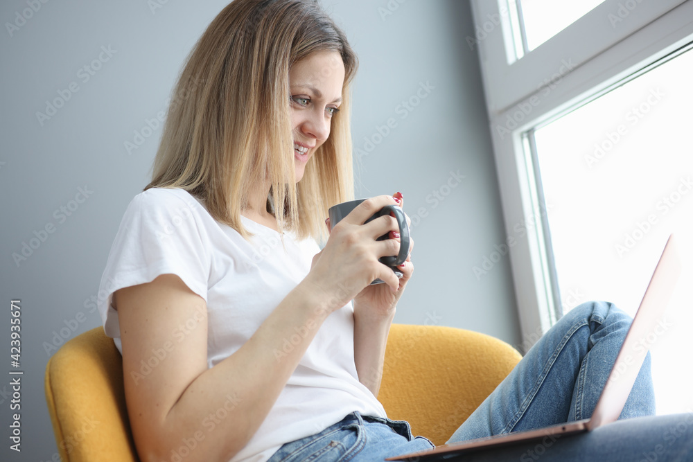 Woman holds cup of coffee and looks into laptop Woman holds cup of coffee and looks into laptop