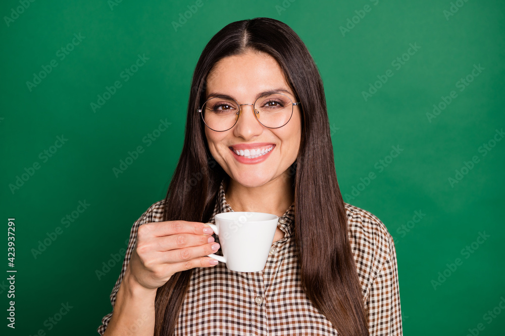 Photo of woman hold cup toothy beaming smile wear eyeglasses checkered shirt isolated green color background Photo of woman hold cup toothy beaming smile wear eyeglasses checkered shirt isolated green color background