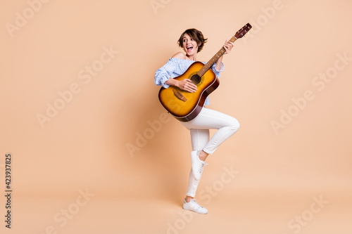 Full size photo of young attractive girl happy positive smile excited play guitar music sing isolated over beige color background