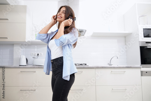 Smiling brunette listening music in headphone in kitchen.