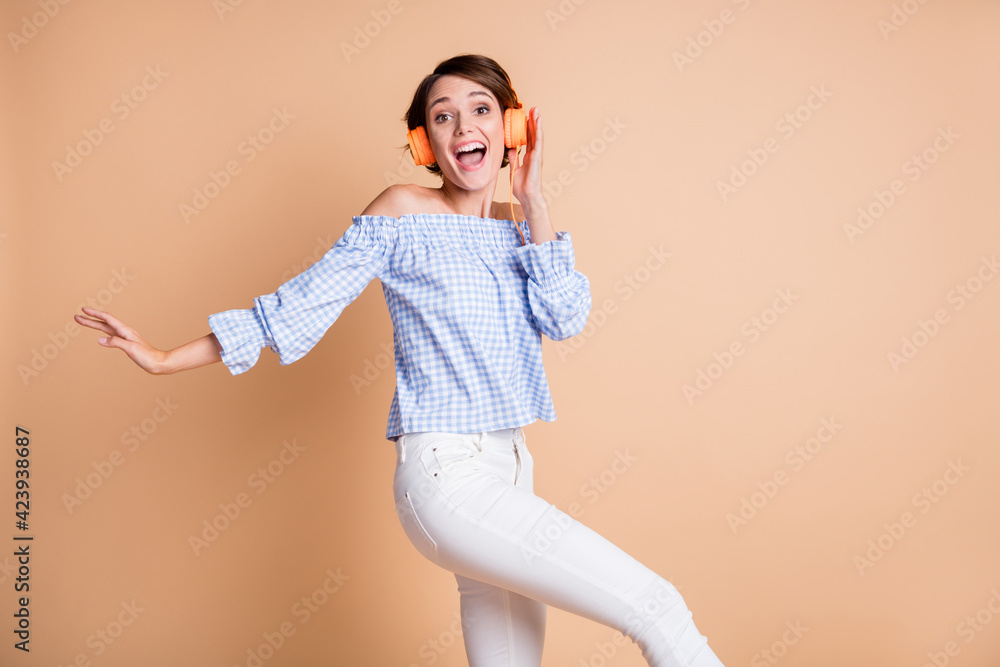 Photo of young excited girl surprised happy positive listen music earphones dance isolated over beige color background Photo of young excited girl surprised happy positive listen music earphones dance isolated over beige color background