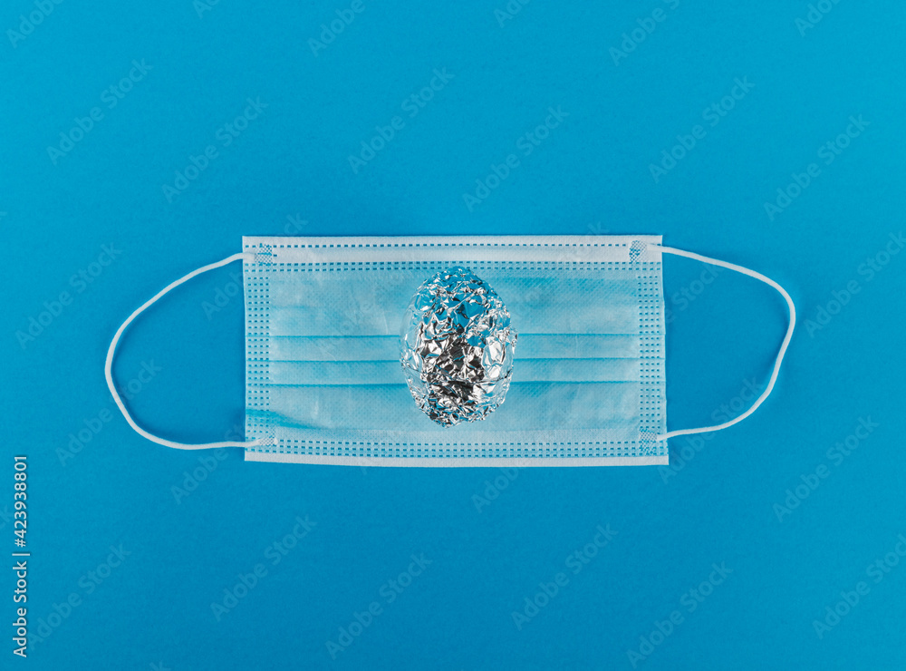 Medical protective mask and Egg in aluminum foil on blue background. Medical protective mask and Egg in aluminum foil on blue background.