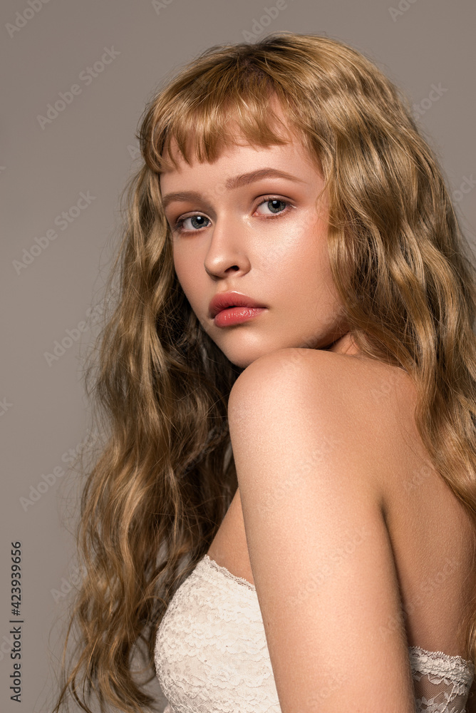 Naklejka premium Close up portrait of young fashion model with beautiful natural blond wavy hair and gentle makeup. The concept of healthy clean well-groomed skin. Trendy hairstyle with bangs cut.