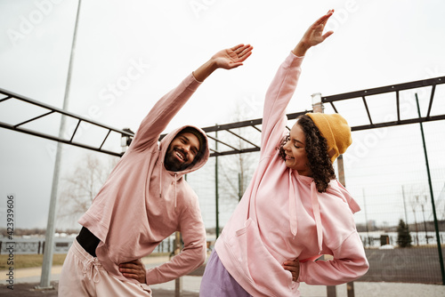 positive african american couple doing side bend exercise outdoors