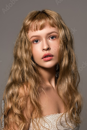 Close up portrait of young fashion model with beautiful natural blond wavy hair and gentle makeup. The concept of healthy clean well-groomed skin. Trendy hairstyle with bangs cut.