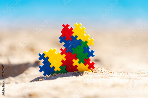 World autism awareness day background. Multicolored puzzle heart on the beach in sunny day