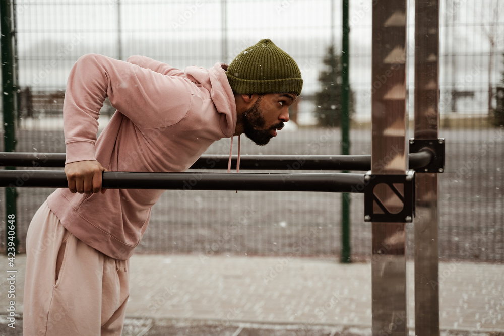 Side view of African American athlete working out on crossbars on stadium outdoors Side view of African American athlete working out on crossbars on stadium outdoors