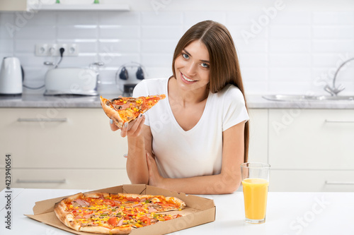 Smiling woman eating tasty pizza in kitchen.