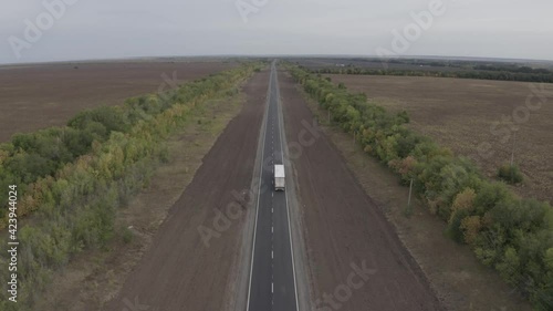 The copter flies over the road, to the left and right of it is a field and a forest, a car is driving along the road