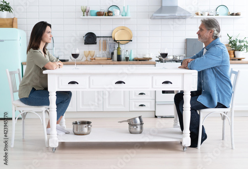 Smiling man and woman chatting, drinking red wine in modern kitchen, happy wife and husband holding glasses