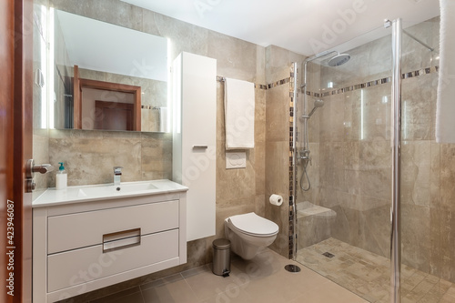 Beige colored bathroom interior  a shower with a glass door and a ceramic toilet  also a few towels on the walls.