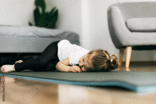 A little girl lies on a yoga mat in the bedroom and rests after a game