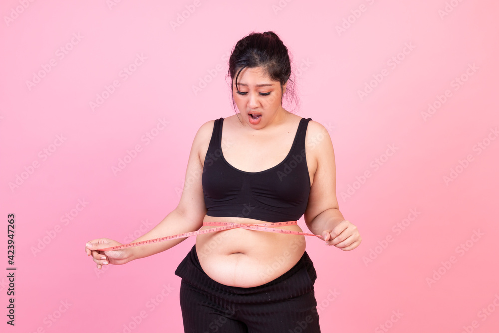 Fat woman with body measures the isolated pink background. Overweight woman measuring her belly fat. Obese female measuring her stomach over pink background. Woman squeeze tighten by measure tape. Fat woman with body measures the isolated pink background. Overweight woman measuring her belly fat. Obese female measuring her stomach over pink background. Woman squeeze tighten by measure tape.