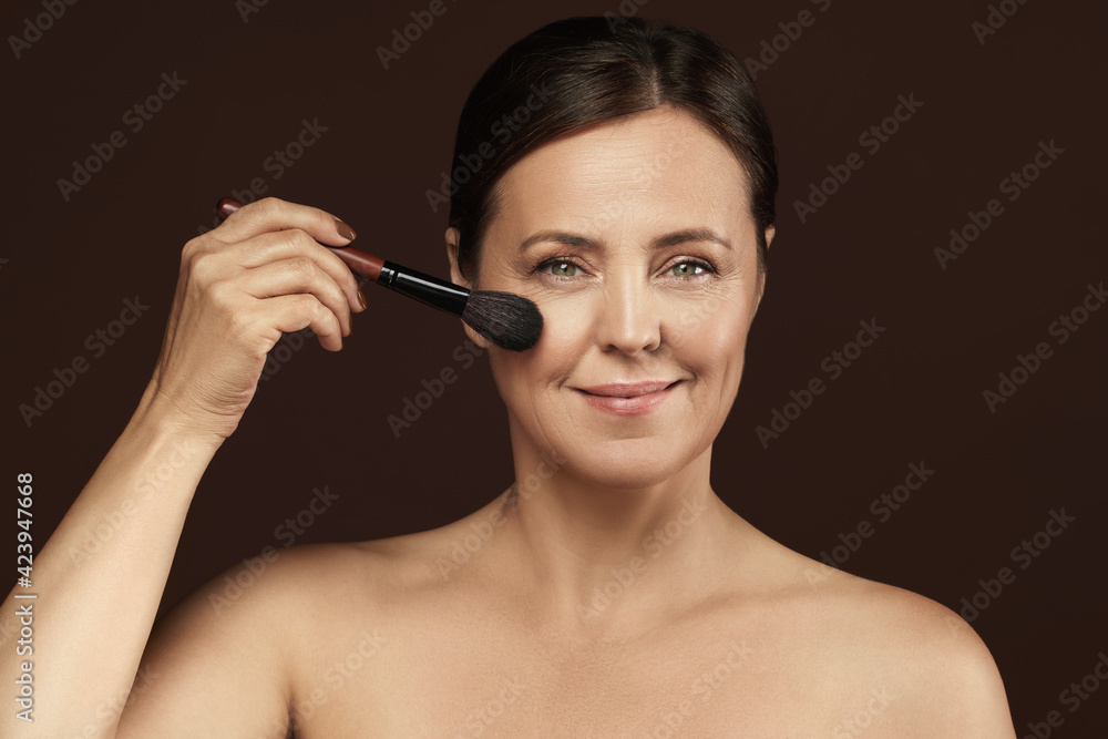 Beautiful middle aged woman with a makeup brush on brown background