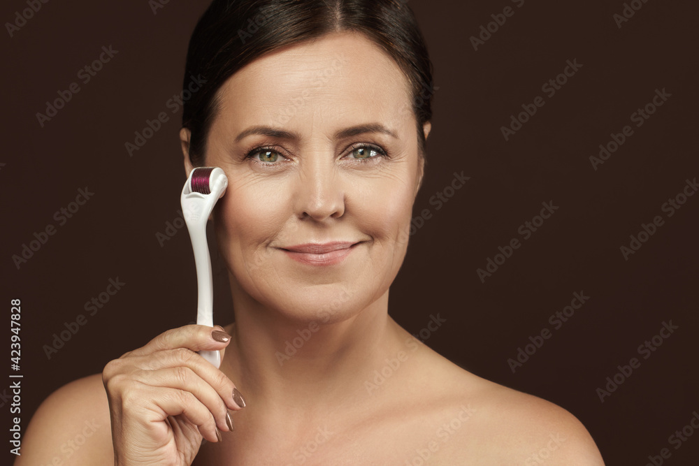 Obraz premium Middle aged woman using mesoroller for her facial skin.