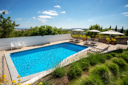 Outdoors shot of a clean pool with some loungers on the side on a clear sunny day.