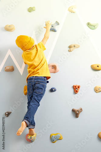 A 3-4-year-old boy is trying to climb a climbing wall and reach for the sun. The concept of striving for high goals