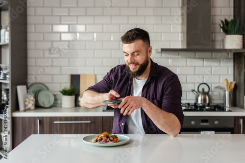 Young Man taking photos of Delicious Food at Home in Modern Kitchen using a Smartphone, Food Blogger working, Portrait, Copy Space