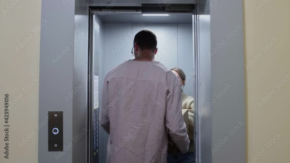 Young happy couple enters in the elevator with cardboard boxes and folding chair moving in to new appartment Young happy couple enters in the elevator with cardboard boxes and folding chair moving in to new appartment