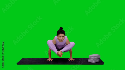 Young woman doing Scale pose while practicing yoga on green screen background  