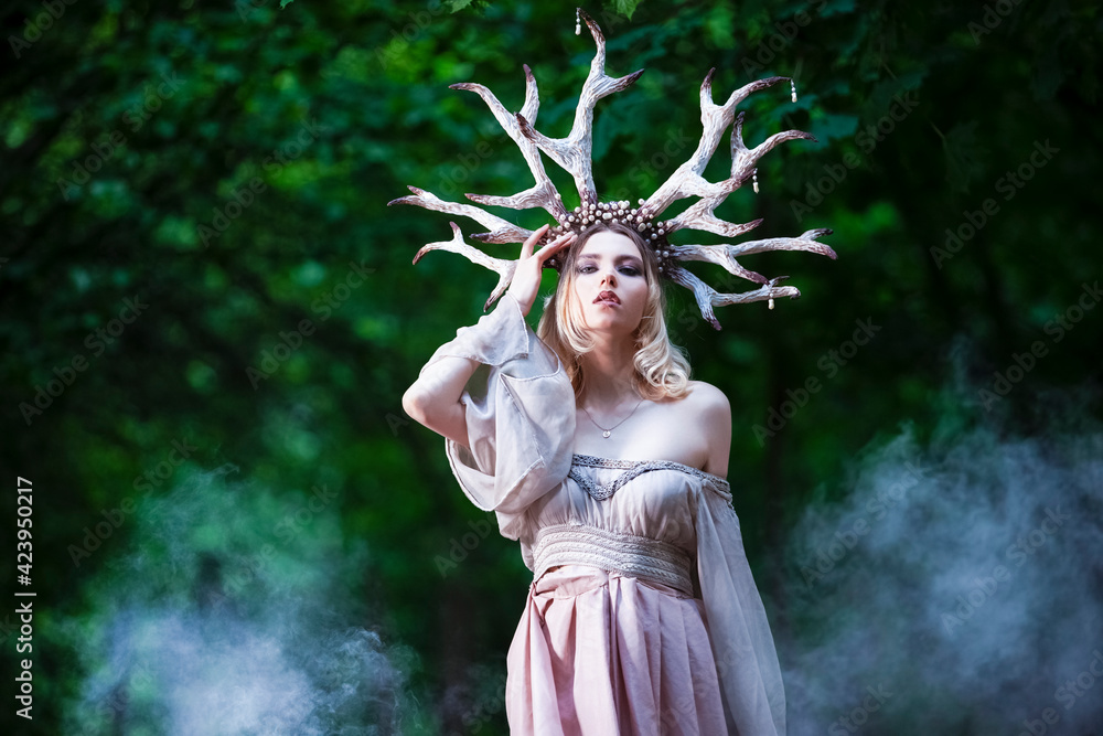 Natural Portrait of Tranquil Caucasian Girl Posing In Light Dress With Artistic Deer Horns In Summer Forest With Grey Smoke Behind.