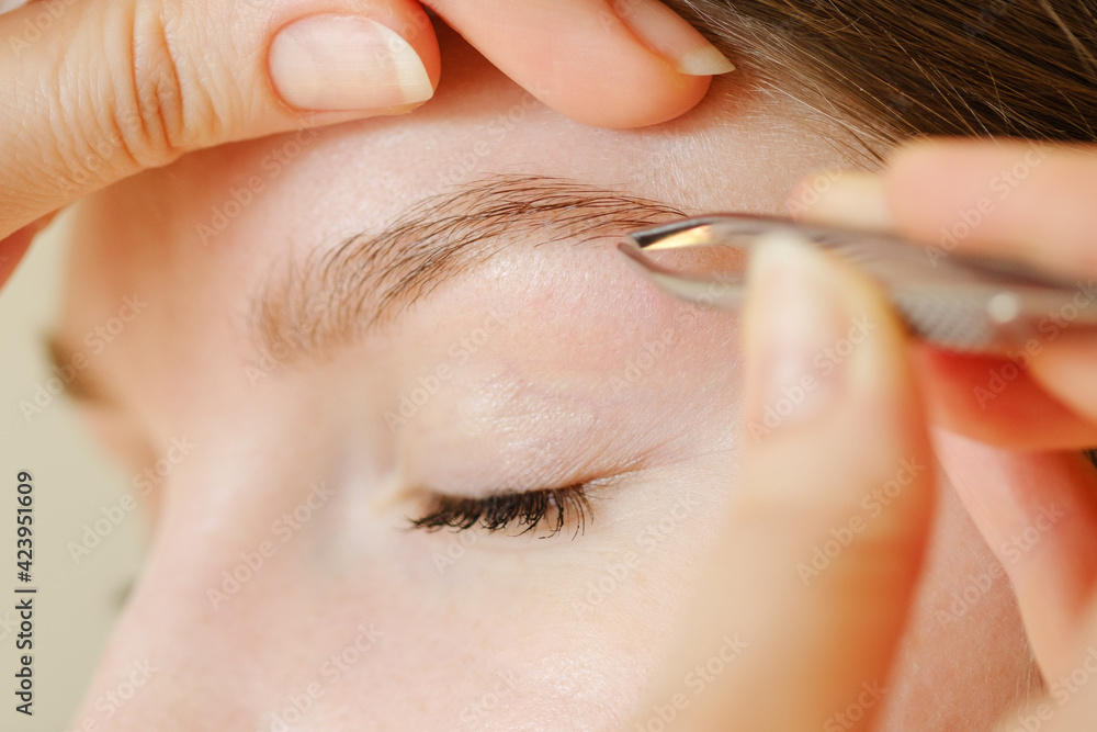 Young caucasian woman getting her eyebrows plucked by her beautician using tweezers. Shallow depth of field