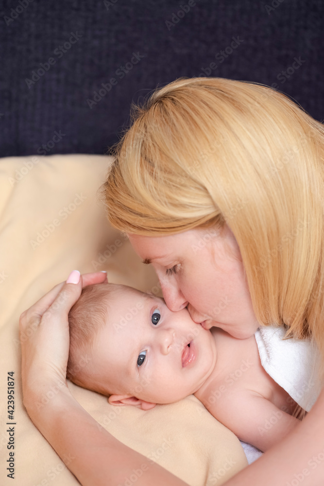 Closeup Portrait of Young Careful Caucasian Mother Kissing and Embracing Her Newborn Baby Boy Lying on Bed. Closeup Portrait of Young Careful Caucasian Mother Kissing and Embracing Her Newborn Baby Boy Lying on Bed.