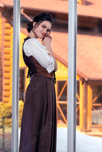 Natural Portrait of Young Brunette Girl Posing in Long Brown Retro Dress In Front of The Window