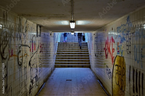 Billede på lærred Some people walk up the steps of a dark and dingy subway tunnel beneath a railwa