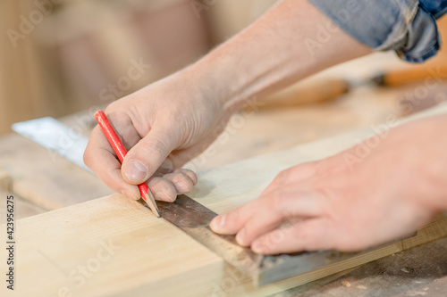 Close up male hands taking measurement of a wooden plank in carpentry workshop