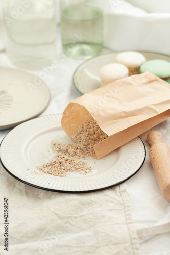 Hazelnut flour. Walnut flour in a paper bag on a light plate with French pastries macaroons in pastel light colors. Ingredients for a pastry shop and bakery