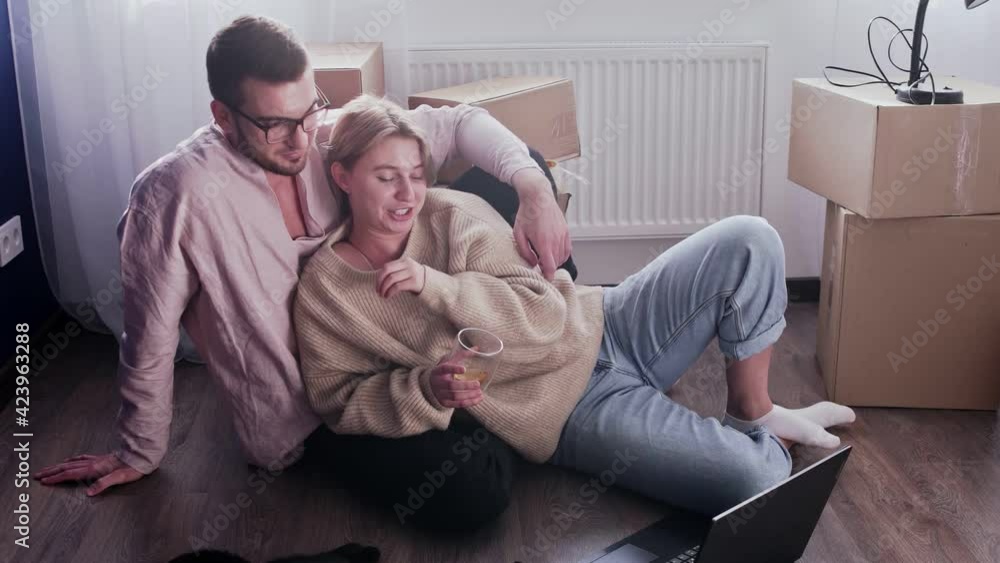 Happy couple relaxes after moving in a new home. Couple sits on floor and watches comedy movie on notebook Happy couple relaxes after moving in a new home. Couple sits on floor and watches comedy movie on notebook