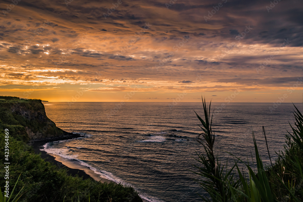 Dramatic and colorful sky in a viewpoint over Viola beach with vegetation and cliff silhouettes, São Miguel - Azores PORTUGAL